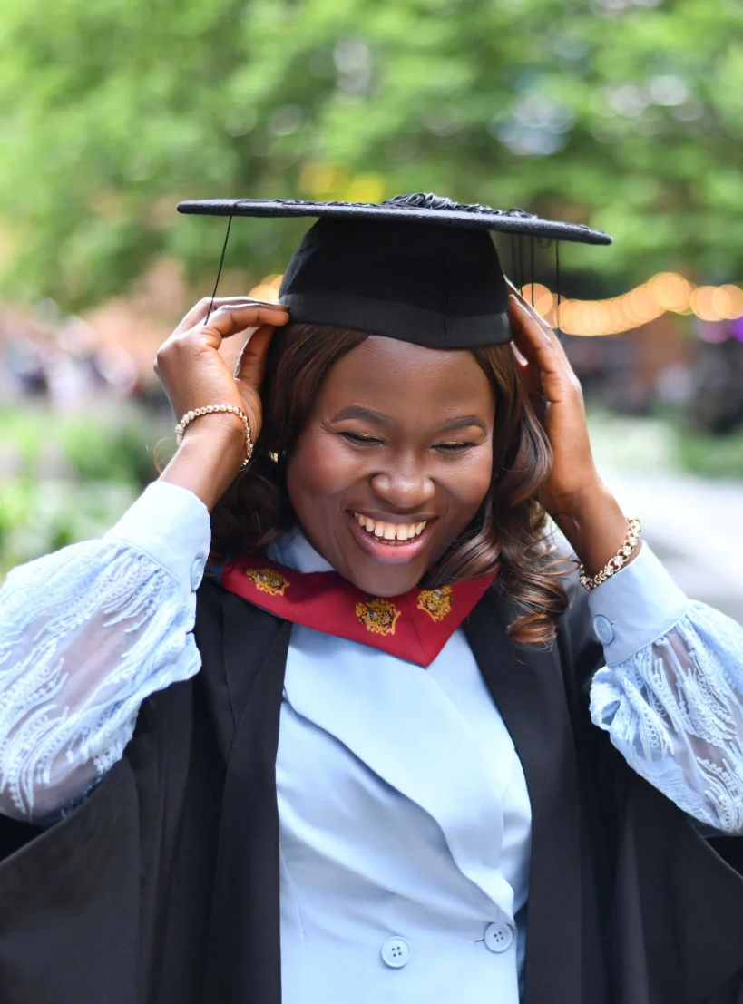 Graduate laughing while adjusting her mortarboard