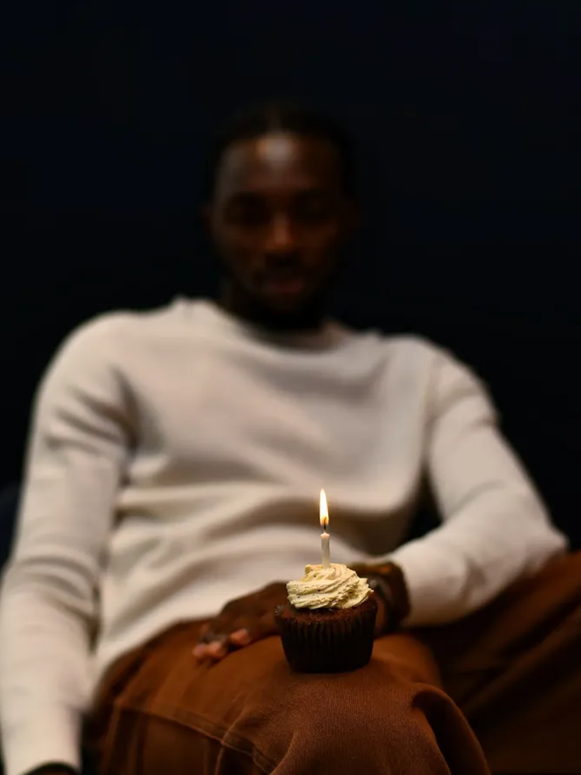 Low-light portrait of a man holding a cupcake with a lit candle