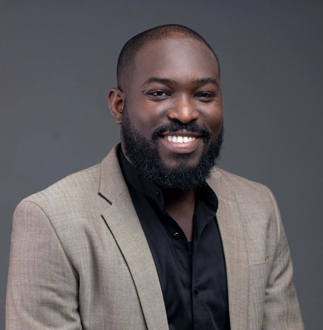 Studio headshot of a smiling man in a tan blazer